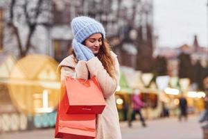 jong meisje in warm kleren met boodschappen doen Tassen in handen hebben een wandelen buitenshuis in de stad foto