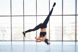 jong sportief vrouw in sportkleding jumping en aan het doen atletisch trucs tegen venster in de lucht foto