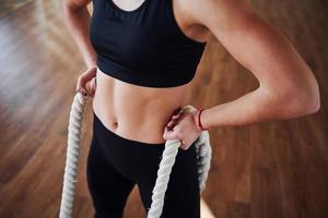 dichtbij omhoog visie van sportief jong vrouw in zwart sportief kleren dat staand met knopen in handen in Sportschool foto