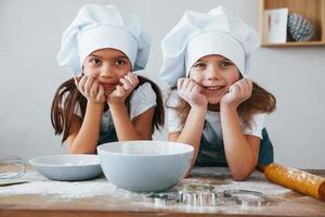 twee weinig meisjes in blauw chef uniform glimlachen samen Aan de keuken foto