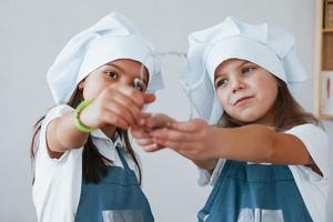 twee weinig meisjes in blauw chef uniform werken met meel Aan de keuken foto