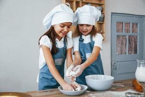 twee weinig meisjes in blauw chef uniform werken met meel Aan de keuken foto