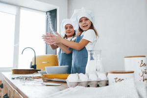 twee weinig meisjes in blauw chef uniform werken met meel Aan de keuken foto