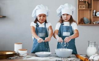 twee weinig meisjes in blauw chef uniform werken met meel Aan de keuken foto