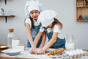 twee weinig meisjes in blauw chef uniform kneden deeg Aan de keuken foto