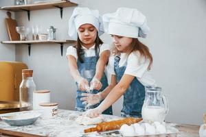 twee weinig meisjes in blauw chef uniform kneden deeg Aan de keuken foto