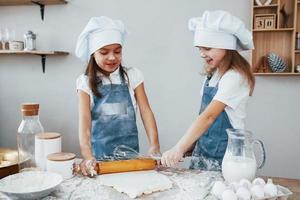 twee weinig meisjes in blauw chef uniform kneden deeg Aan de keuken foto