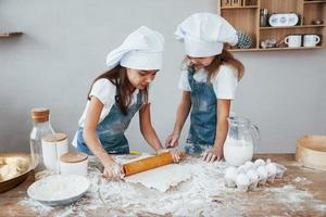 twee weinig meisjes in blauw chef uniform kneden deeg Aan de keuken foto