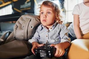 kinderen in gewoontjes kleren zittend samen met controleur en spelen video spellen foto