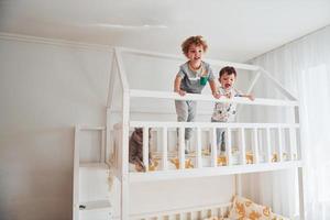 twee weinig jongens resting en hebben pret binnenshuis in de slaapkamer samen. kat zittend in de buurt hen foto