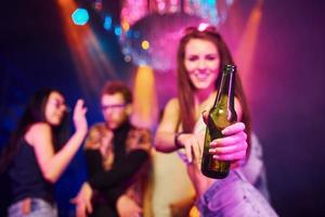 meisje Holding fles. jong mensen is hebben pret in nacht club met kleurrijk laser lichten foto