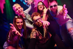 gaan gek en poseren voor de camera samen. jong mensen is hebben pret in nacht club met kleurrijk laser lichten foto