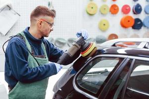 mannetje arbeider in uniform polijsten nieuw modern auto. opvatting van onderhoud foto