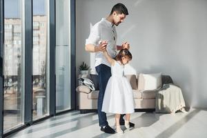 gelukkig vader met zijn dochter in jurk aan het leren hoe naar dans Bij huis samen foto