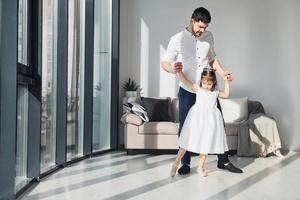 gelukkig vader met zijn dochter in jurk aan het leren hoe naar dans Bij huis samen foto