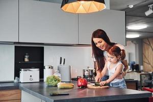 moeder met haar weinig dochter snijden groenten binnenshuis in keuken foto