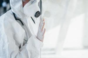 voelt slecht en ziek. vrouw dokter wetenschapper in laboratorium jas, defensief eyewear en masker staand binnenshuis foto