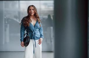 aantrekkelijk vrouw in blauw overhemd en wit broek binnenshuis poseren voor een camera. in luchthaven of auto winkel foto