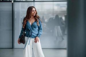 aantrekkelijk vrouw in blauw overhemd en wit broek binnenshuis poseren voor een camera. in luchthaven of auto winkel foto