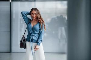 aantrekkelijk vrouw in blauw overhemd en wit broek binnenshuis poseren voor een camera. in luchthaven of auto winkel foto