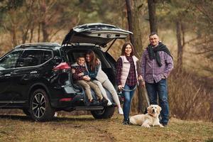 gelukkig familie hebben pret met hun hond in de buurt modern auto buitenshuis in Woud foto