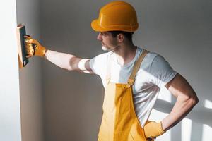 klusjesman in geel uniform polijsten muur binnenshuis. huis vernieuwing opvatting foto