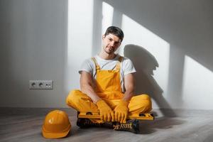 moe klusjesman in geel uniform zit binnenshuis en duurt pauze. huis vernieuwing opvatting foto