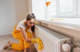 huisvrouw in geel uniform werken met venster en oppervlakte schoonmaakster binnenshuis. huis vernieuwing opvatting foto