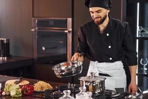 professioneel jong chef koken in uniform frituren voedsel Aan de keuken foto