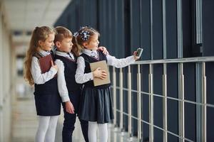school- kinderen in uniform samen met telefoon en maken selfie in hal. opvatting van onderwijs foto