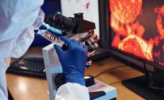 wetenschapper in wit beschermend slijtage binnenshuis in laboratorium met lens met virus titel Aan het foto