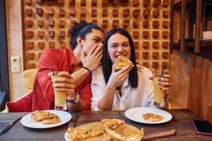 multi etnisch jong paar zittend binnenshuis samen en aan het eten pizza foto