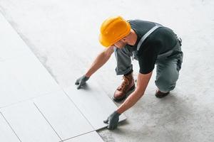 installatie van platen. Mens in grijs uniform en oranje moeilijk hoed werken binnenshuis in modern groot kantoor Bij dag foto