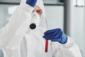 mannetje dokter wetenschapper in laboratorium jas, defensief eyewear en masker werken met test buis met bloed binnen van het foto