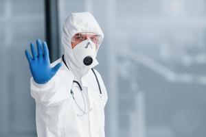 shows hou op gebaar door hand. mannetje dokter wetenschapper in laboratorium jas, defensief eyewear en masker foto
