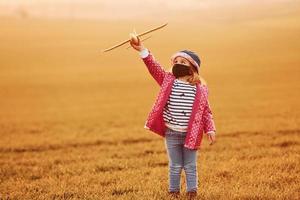 verlichte door oranje gekleurde zonlicht. schattig weinig meisje hebben pret met speelgoed- vlak Aan de mooi veld- Bij dag foto