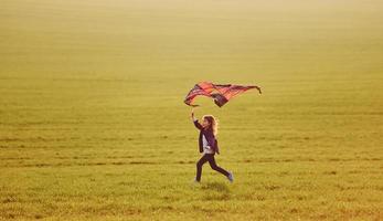 gelukkig weinig meisje rennen met vlieger in handen Aan de mooi veld- foto