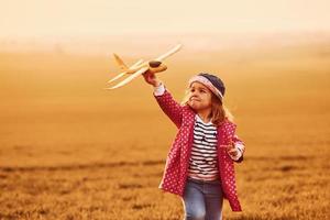 verlichte door oranje gekleurde zonlicht. schattig weinig meisje hebben pret met speelgoed- vlak Aan de mooi veld- Bij dag foto