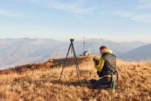 mannetje fotografen staand en werken Bij majestueus landschap van herfst bomen en bergen door de horizon foto