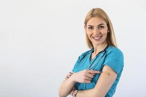 jong dokter, medisch arbeider richten Bij haar arm met een verband na ontvangen de covid-19 vaccin. jong verpleegster tonen haar schouder na krijgen coronavirus vaccin foto