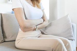 vrouw aan het liegen Aan sofa op zoek ziek in de leven kamer. mooi jong vrouw aan het liegen Aan bed en Holding handen Aan haar maag. vrouw hebben pijnlijk maagpijn Aan bed, menstruatie- periode foto