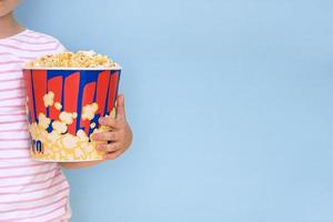 kind Holding groot papier kop met popcorn Aan blauw achtergrond met kopiëren ruimte foto