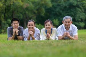 portret van groep van Aziatisch familie met vader, moeder, zoon en dochter aan het liegen naar beneden samen Aan de gras gazon Bij de openbaar park gedurende weekend werkzaamheid voor recreatie en welzijn concept foto