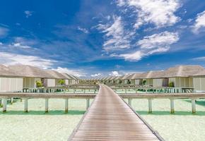 Maldiven eiland strand panorama. luxe water villa's lang houten pier pad. tropisch vakantie en zomer vakantie achtergrond concept. verbazingwekkend landschap met kopiëren ruimte foto