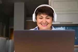 voorkant visie Bij ouderling vrouw in haar Jaren 50 met koptelefoon gebruik makend van laptop voor onderwijs, werk, online winkelen, luisteren naar podcast, enz foto