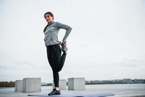 jong sportief meisje aan het doen yoga opdrachten Aan geschiktheid mat buitenshuis in de buurt meer Bij dag foto