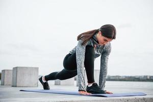 jong sportief meisje aan het doen yoga opdrachten Aan geschiktheid mat buitenshuis in de buurt meer Bij dag foto