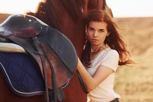 jong vrouw omarmen haar paard in landbouw veld- Bij zonnig dag foto