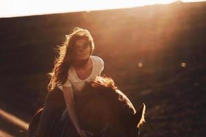 jong vrouw in beschermend hoed met haar paard in landbouw veld- Bij zonnig dag foto