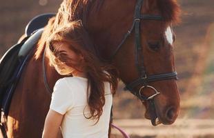 jong vrouw omarmen haar paard in landbouw veld- Bij zonnig dag foto